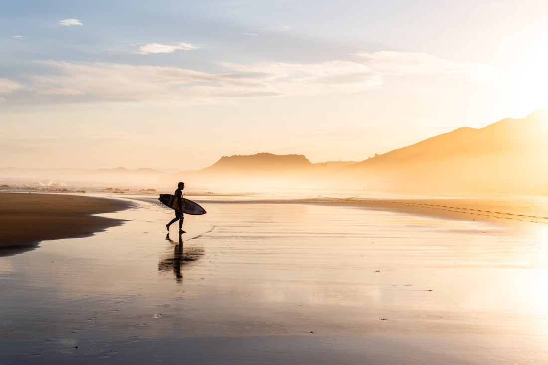 Lone surfer walking on the sand at Wainui Beach in Gisborne