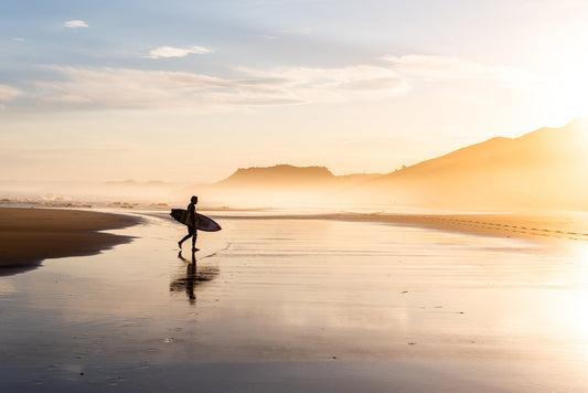 Lone surfer walking on the sand at Wainui Beach in Gisborne
